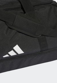 Crna sportska torba izrađena od izdržljive tkanine, s podesivim trakama i detaljem bijelog loga. Kompaktni dizajn sa zatvaranjem na patentni zatvarač.