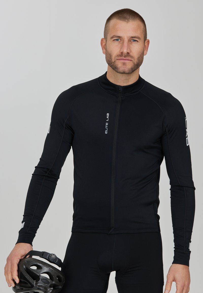 Schwarzes Langarm-Radtrikot mit Reißverschluss, ausgestattet mit einer taillierten Passform, glatter Oberfläche und reflektierenden Akzenten. Ein schwarzes Helm wird in der Hand gehalten.