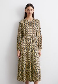 Langärmliges, knielanges Kleid aus gemustertem Stoff in gelben, braunen und grauen Quadraten. Am Bund mit einem passenden Gürtel befestigt.
