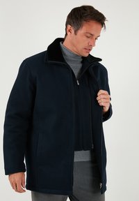 Jūras spēku zilas krāsas jaka ar mīkstu, strukturētu virsmu, ar kažokādas oderi apkaklē, priekšējo rāvējslēdzēju un sānu kabatām. Klasisks dizains ar brīvu piegriezumu.