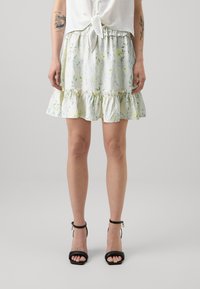 Skjorte med blomsterprint, lett stoff, rynket kant, elastisk midje og myk tekstur i pastellfarger, iført med svarte ankelrem sandaler.