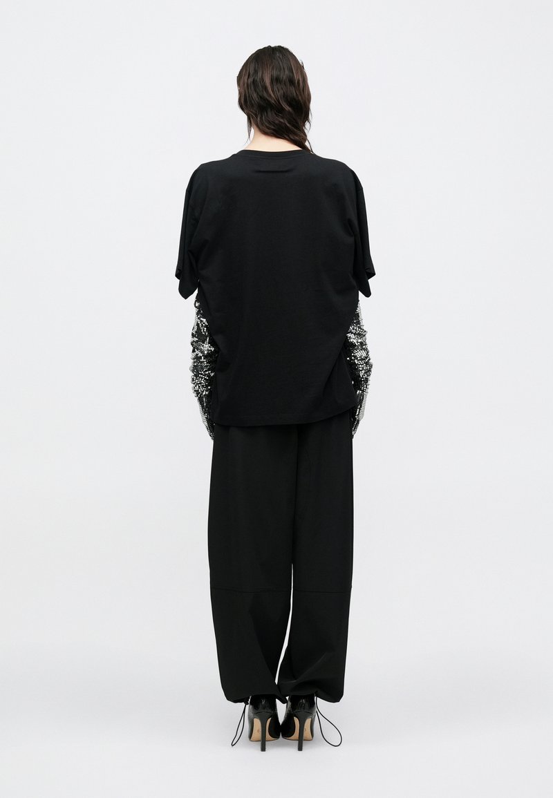 Sort oversized T-shirt med korte ærmer, der har teksturerede pailletdetaljer på siderne. Kombineret med løse sorte bukser og højhælede sko.