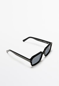Czarne prostokątne okulary przeciwsłoneczne z ciemnymi soczewkami, błyszczącą plastikową oprawką i zwężanymi ramionami z subtelnymi metalowymi akcentami.