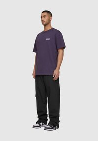 Lilla bomulds t-shirt med rund hals og korte ærmer, parret med sorte cargo bukser og sort-hvide sneakers.