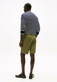 Maglione a righe navy e bianche, pantaloni corti verde oliva, mocassini neri, visto da dietro. Maglia a treccia con polsini e vita a coste.