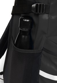 Poche noire d'un sac à dos contenant une bouteille noire. La poche présente un design en maille avec une bande argentée contrastante sur le côté.