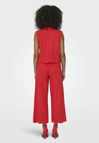 Completo rosso a due pezzi composto da un top senza maniche con motivo a occhiello e pantaloni a gamba larga, entrambi con orli ondulati e dettagli a intaglio.