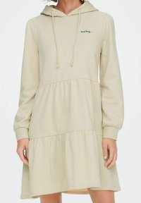 Vestido sudadera beige claro con mangas largas, diseño en capas y texto frontal "low key...". Está hecho de material suave. Presenta una capucha con cordones.
