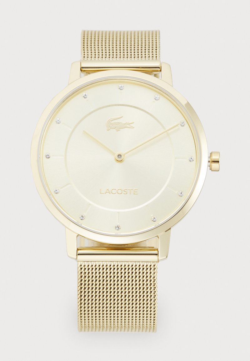 Gold-tone watch with a mesh band. Features a pale yellow dial with a crocodile logo, crystal hour markers, and simple hour and minute hands.
