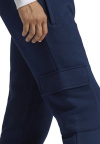 Marineblaue Cargo-Hosen mit einer weichen Textur, ausgestattet mit einer Seitentasche mit Klappenverschluss und einem figurbetonten Design. Sichtbare Nähte heben das Ganze hervor.