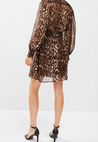 Brązowa sukienka w leopardzie w czarnym kolorze z długimi rękawami, marszczonym pasem, przezroczystą teksturą i rozkloszowanym dołem. W zestawie z czarnymi sandałami na wysokim obcasie.