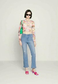 Top cropped de manga longa com um padrão de colagem multicolorido; jeans de ganga azul claro com acentos desgastados; saltos abertos de cor rosa brilhante; bolsa verde.