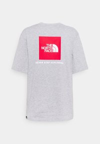 Světle šedé tričko s krátkým rukávem s červeným čtvercovým logem na zadní straně, které říká "The North Face" a bílým textem níže, který zní "Never Stop Exploring."