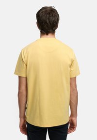 Geel katoenen t-shirt met korte mouwen, ronde halslijn en een rechte snit. Bevat een klein zichtbaar etiket aan de onderzijde.