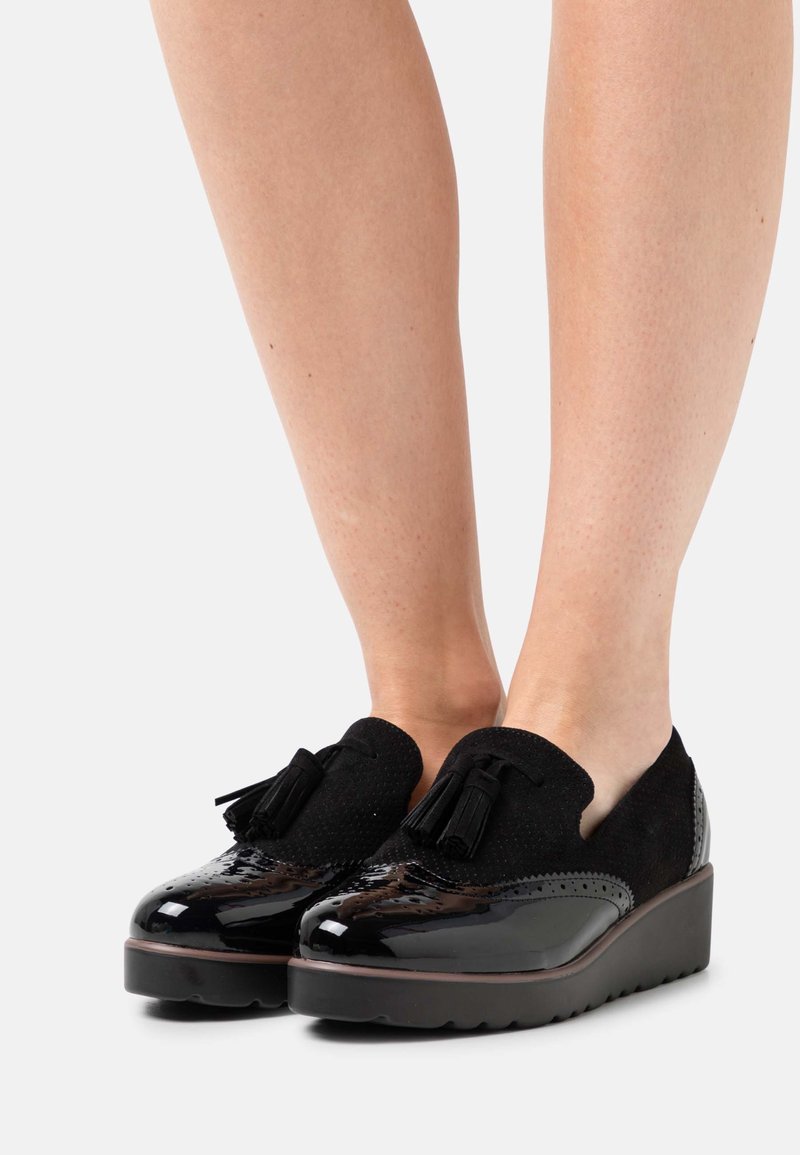 Escarpins compensés en cuir verni noir avec des accents en daim et des franges décoratives, mettant en avant un bout arrondi et une tige texturée.