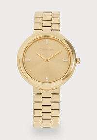 Gold-tone analog wristwatch with a smooth circular case, a matte gold dial, quartz movement, and five crystal hour markers on a metal bracelet.