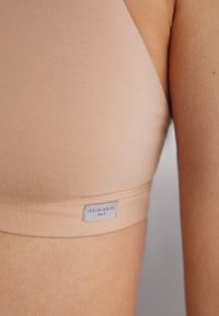 Beige wireless bra made of soft fabric with a seamless design. Features a logo label on the band and a smooth texture.
