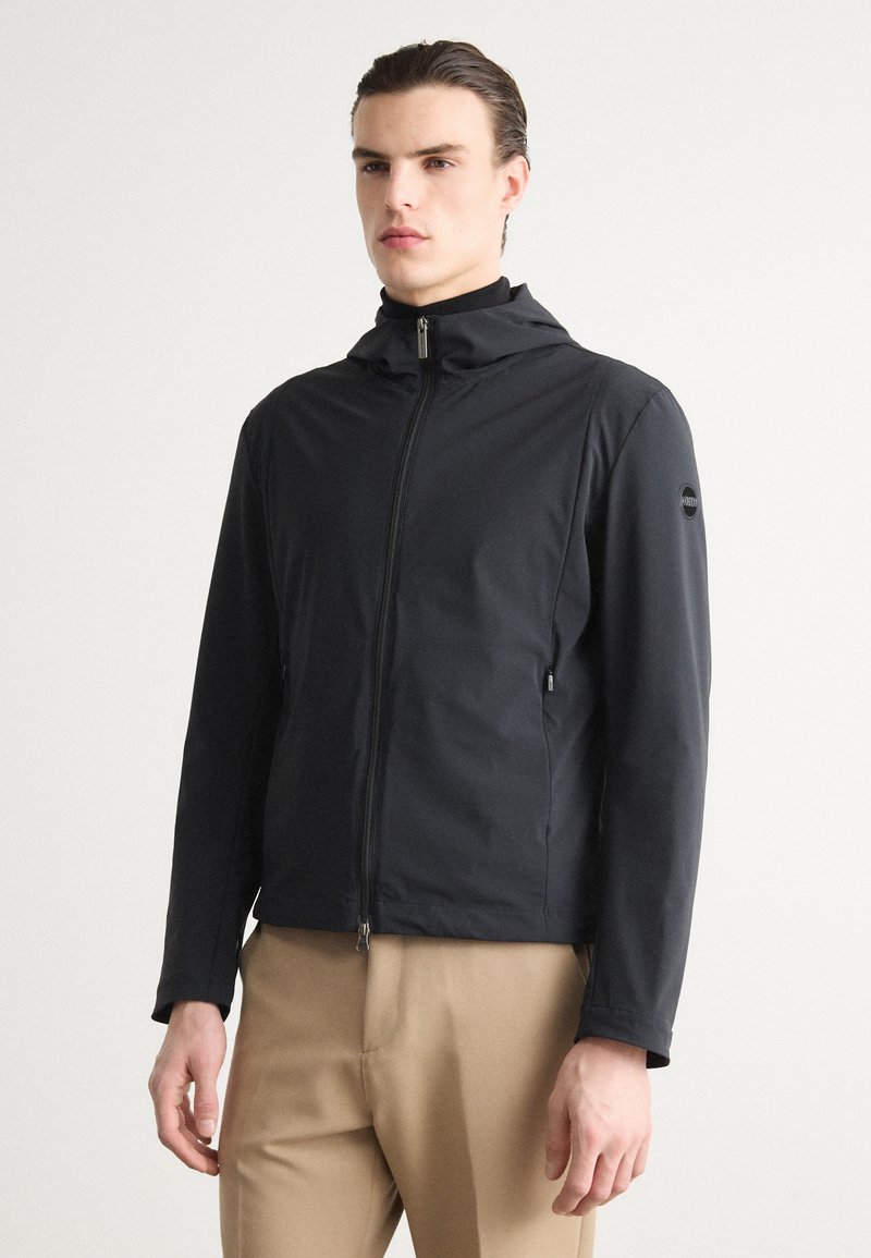 Black hooded jacket with a zip closure, featuring a smooth, matte texture and a logo patch on the left sleeve. Fitted design with pockets.