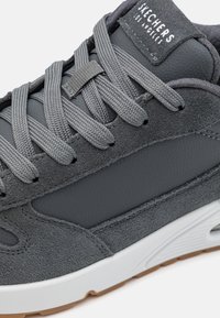 Gray suede and leather sneaker with gray laces, a padded tongue, and a white rubber outsole. Features textured accents for grip.