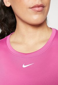 Top deportivo rosa con escote redondo. Presenta una tela suave y elástica, y un logotipo de Nike blanco situado en el centro del pecho.