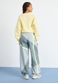 Yellow sweatshirt with dropped shoulders, gray pants featuring geometric patterns and neon accents, paired with white and gray sneakers.
