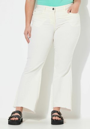 Jeans blancos acampanados con dobladillo sin acabar, bolsillos frontales y cierre con botón, combinados con sandalias de plataforma negras con hebillas doradas.