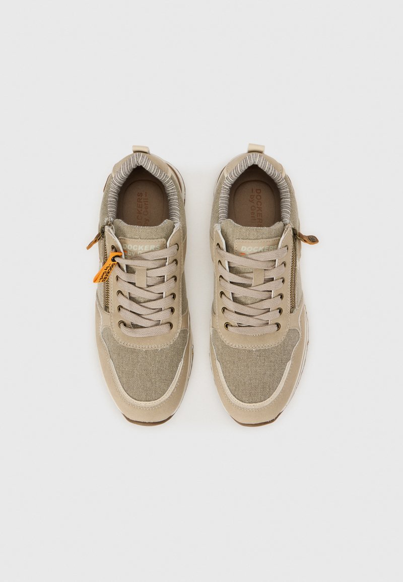 Zapatillas beige con parte superior de tela y acentos en gris claro en contraste. Cuenta con suela de goma, cordones y un detalle lateral con cremallera.