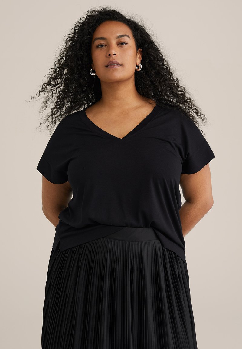 T-shirt nera a V con tessuto morbido, con maniche corte e vestibilità rilassata. Abbinato a una gonna nera plissettata.