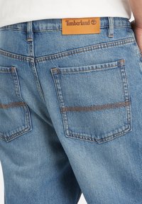 Džínové kalhoty s prostředním zesvětlením a koženou nášivkou Timberland, mají dvě zadní kapsy s kontrastním prošíváním a volný střih.