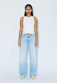 Light blue wide-leg jeans paired with a white sleeveless top; smooth fabric, casual design, minimalistic style, contrasting footwear detail.