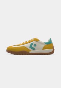 Sneaker with a yellow suede upper, white leather accents, and a turquoise star logo. Features a textured rubber sole and lace-up design.