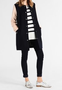 Granatowo-różowa długa kurtka z zaokrąglonym kołnierzem, srebrne guziki, czarno-biała paskowana bluzka, czarne spodnie i metaliczne buty.