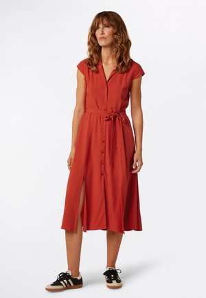 Rode jurk met korte mouwen, knoopsluiting, tailleband, zijsplitsen en een subtiel patroon, gecombineerd met zwart-crème sportieve sneakers.