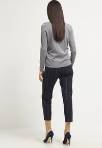 Harmaa pitkähiha pusero yhdistettynä laivastonsinisillä pystyraidoilla koristeltuihin housuihin ja laivastonsinisiin stiletto-koroihin. Sileä pinta, istuva muotoilu, nilkkapituiset housut.