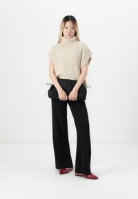 Beige fuzzy gebreid top met een hoge kraag, gecombineerd met zwarte wijde broek en een verzamelde zwarte pouch tas. Rode instappers met accenten.