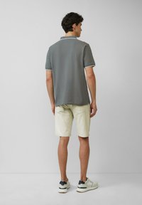 Grijze polo met korte mouwen en contrasterende kraag, gecombineerd met lichtbeige shorts en witte sneakers, gezien van achteren.