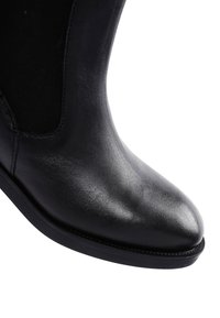 Bottine en cuir noir avec une finition lisse, des panneaux latéraux élastiques et un design à bout rond. Semelle en caoutchouc solide avec des détails de couture subtils.