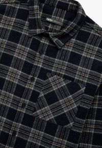 Koszula flanelowa w ciemnogranatowym kolorze z wzorem w kratę w odcieniach szaro-brązowych, z kołnierzykiem typu spread, z przodu na guziki oraz jedną kieszenią na piersi.