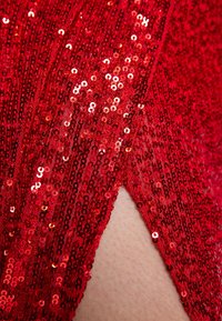 Nahaufnahme eines roten Pailletten-Stoffes mit einem Schlitz, der die darunterliegende Haut enthüllt.