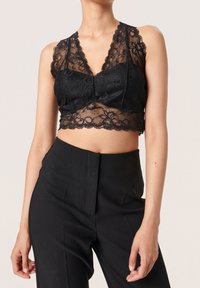 Bralette de encaje negro con patrón floral, bordes festoneados y escote en V profundo. Combinado con pantalones negros de talle alto.