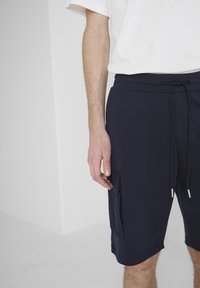 Pantalones cortos de algodón azul marino con cintura elástica, cierre con cordón y un bolsillo lateral. La tela parece suave con una textura lisa.