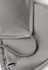 Tissu rembourré gris avec des coutures renforcées, de petites perles décoratives et une boucle élastique, probablement partie d'un article portable ou accessoire.