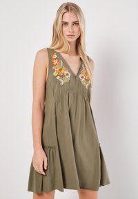 Abito senza maniche verde oliva con scollatura a V, dettagli floreali ricamati in arancione e blu, vita arricciata e gonna svasata con tasche laterali.