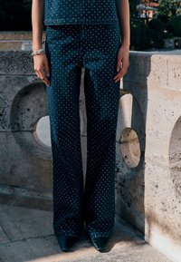 Tumedast teksast laiade säärtega püksid, millel on valged täpid, lõdvestunud istuvus ja mida on kombineeritud terava ninaga kontsadega. Esile tõstetud tekstuuriga pind.