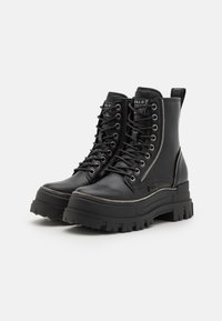Botas de combate negras con una plataforma gruesa, que presentan un upper de cuero texturizado, cierre de cremallera y acentos de metal.