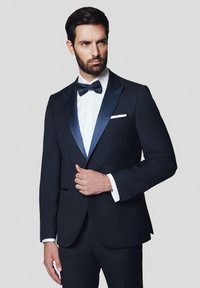 Granatowy smoking z satynowymi klapami, biała koszula, czarny muszka i poszetka; dopasowany krój z detalami na guzikach i mankietach.