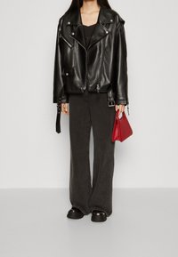 Black leather biker jacket with silver hardware, paired with loose dark gray trousers and shiny black platform shoes. Holding a small red bag.
