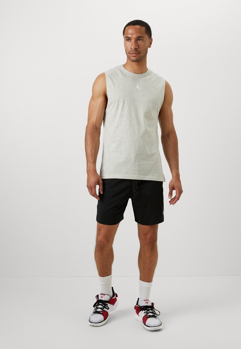 Grå ermeløs skjorte med logo, kombinert med svarte shorts. Antrekket blir komplementert av hvite sokker og rødt-akkenterte joggesko.