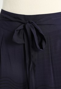 Marinblå midjekjol i lätt tyg med en slät textur och subtilt horisontellt mönster nära fållen.