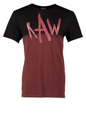 Mężczyzna idący, ubrany w czarną kurtkę z kapturem, ciemnobrązowy t-shirt z nadrukiem, wyblakłe niebieskie dżinsy i czarne skórzane buty na sznurowadła.